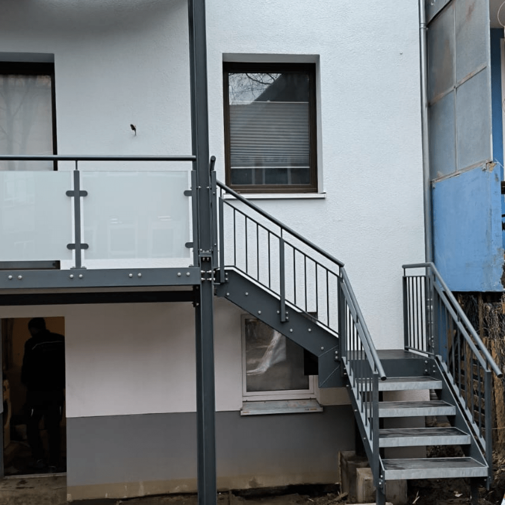 Exterior of a modern gray building with an outdoor metal staircase and glass railing to the upper level.